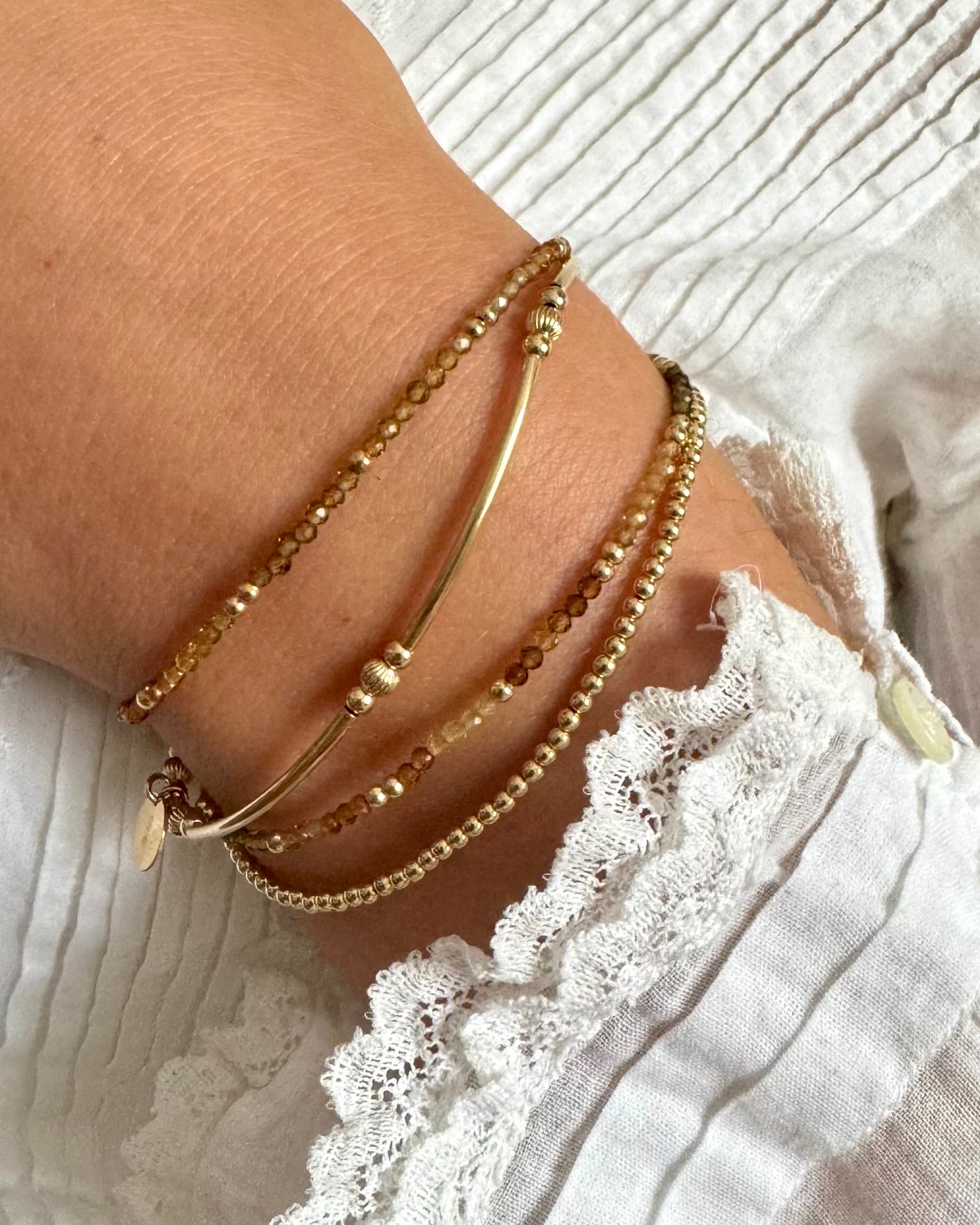 Gold bracelets on a wrist with a white lace garment in the background