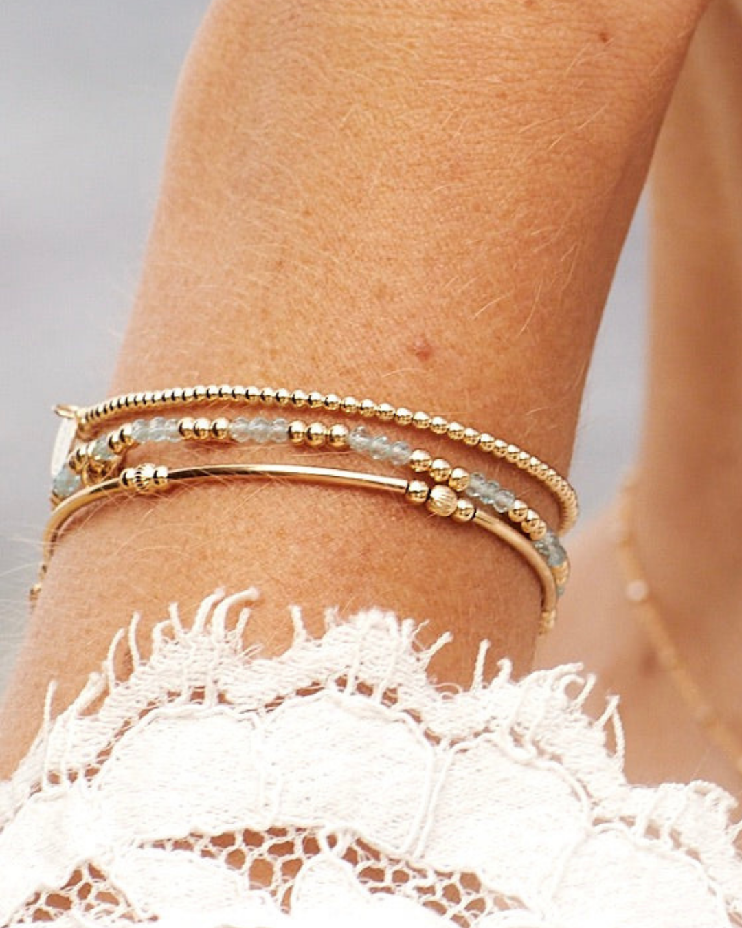 Gold stacked beaded bracelets on a wrist with a blurred background