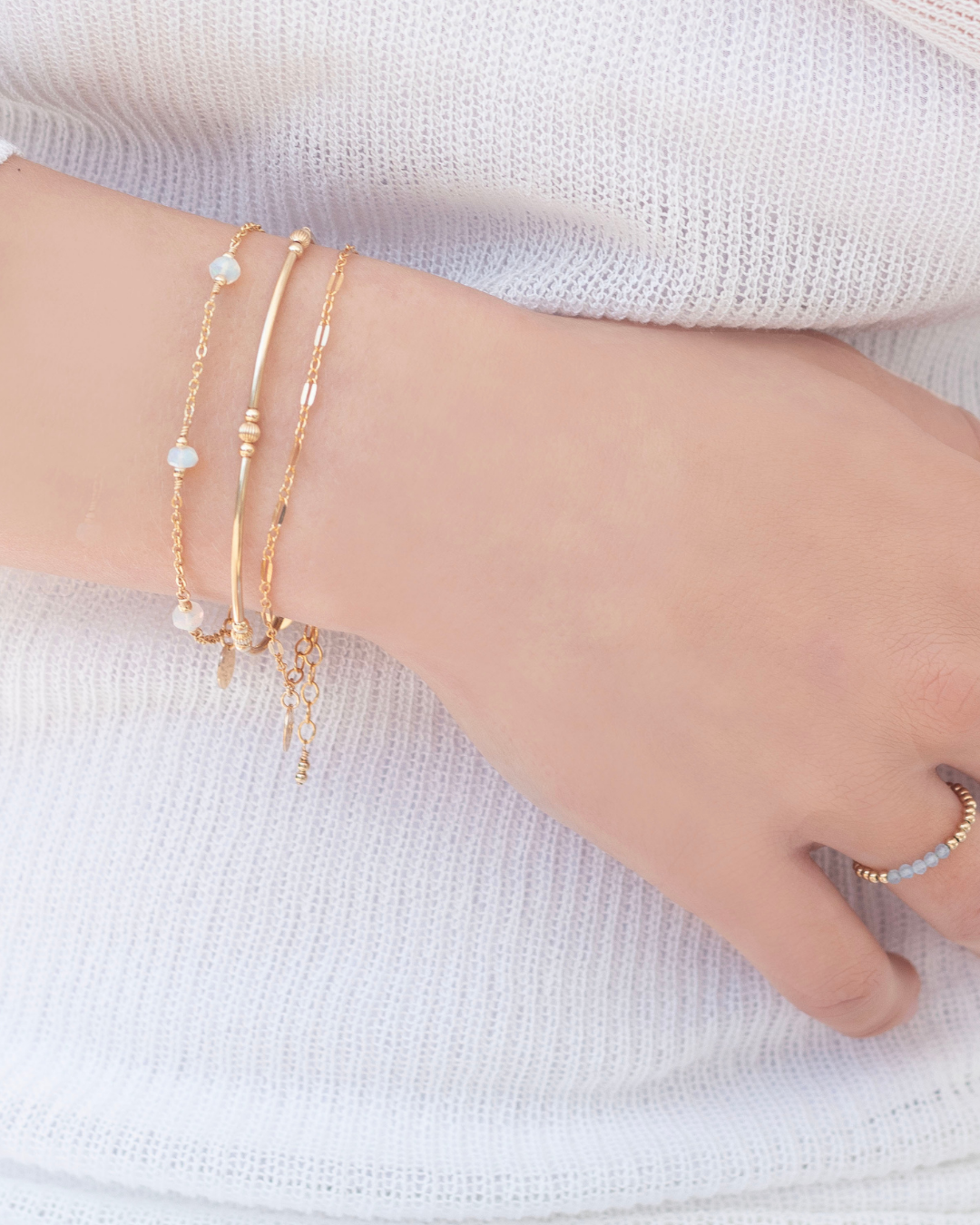 Close-up of a models hand wearing multiple gold bracelets on a light background