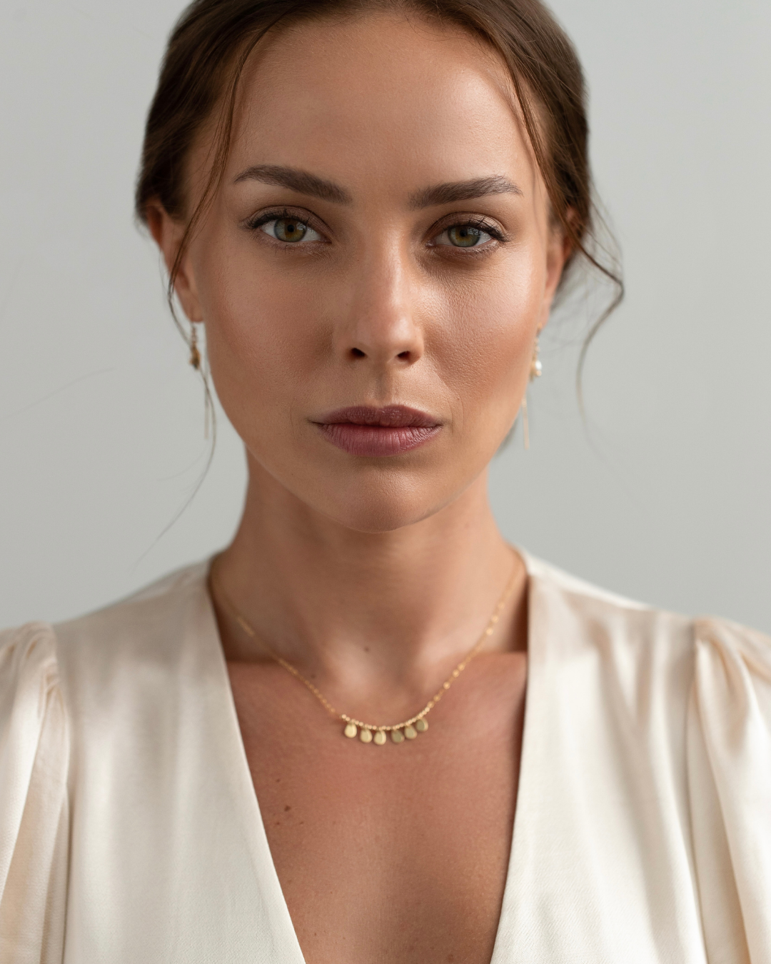 Woman wearing a gold necklace with gold teardrop pendants against a plain background