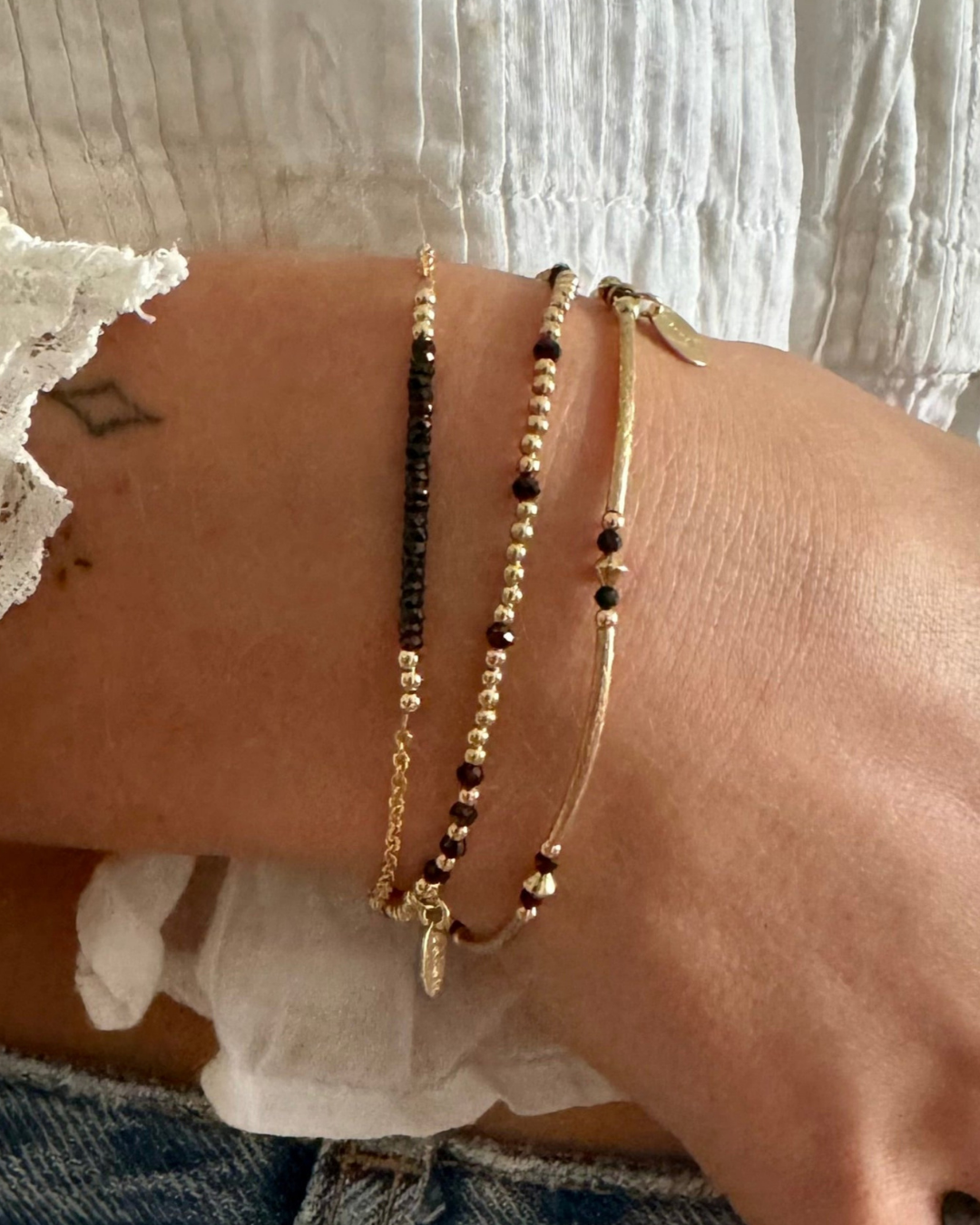 Close-up of a wrist wearing three gold and black spinel beaded bracelets.