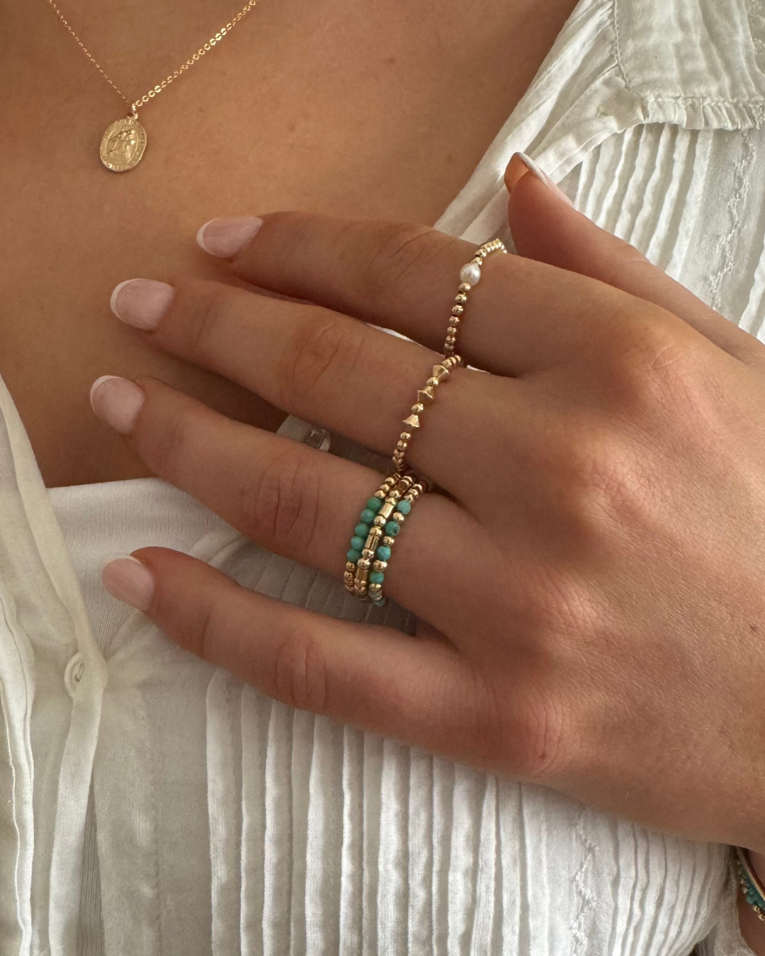 Close-up of a hand wearing gold rings with gold beads and turquoise stones.