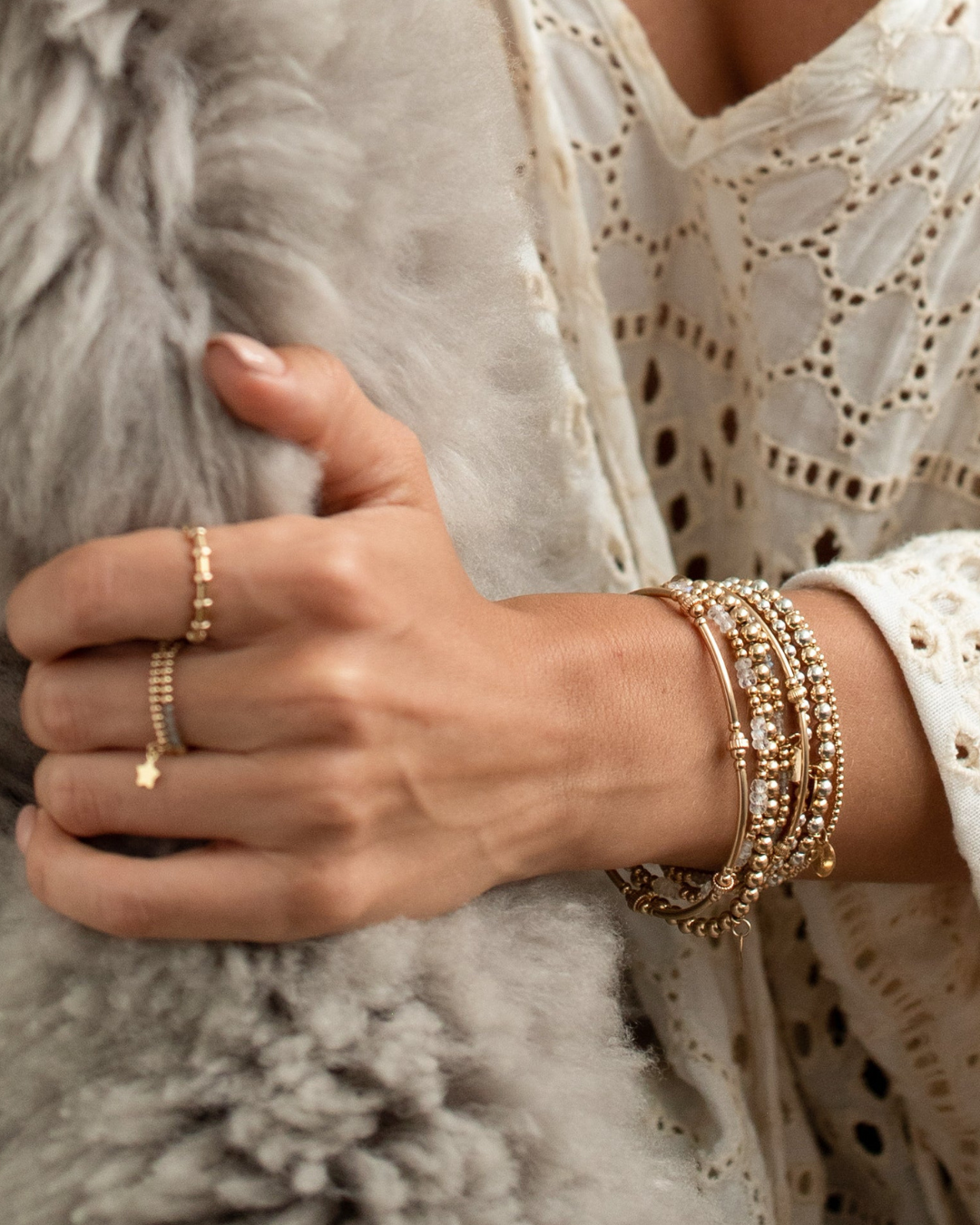 Close-up of a wrist wearing gold beaded bracelets and rings