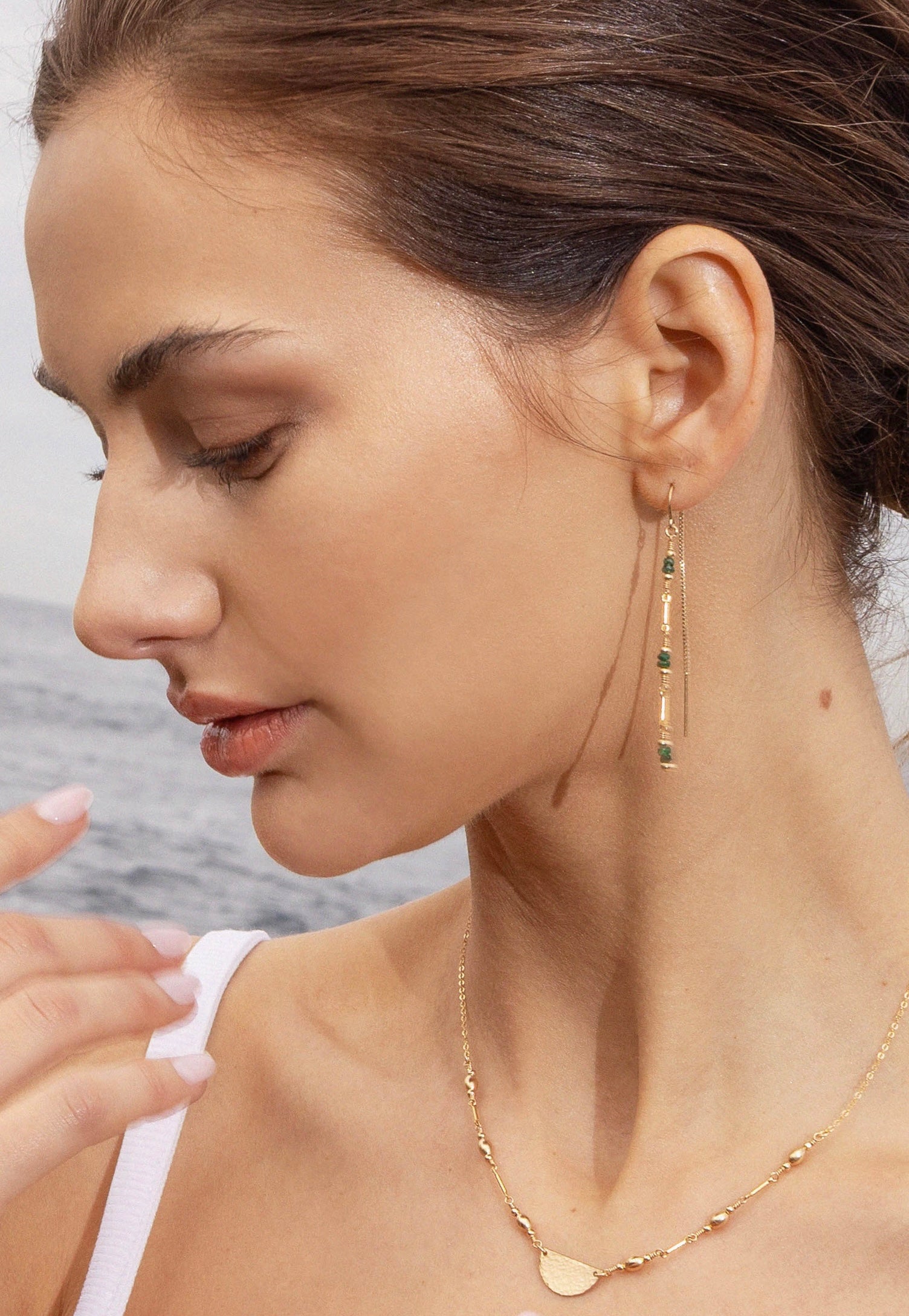 Woman wearing gold earrings with emerald beads and gold necklace with a blurred background