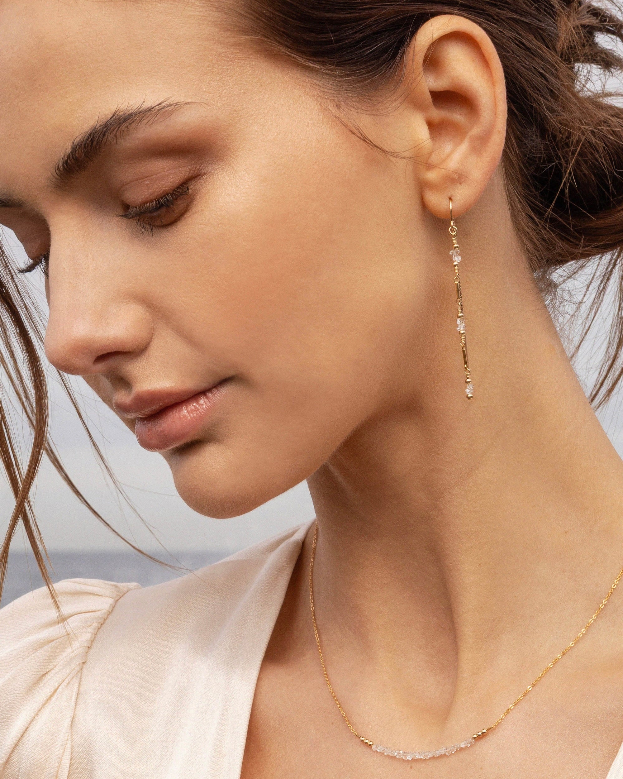 Close-up of a woman wearing gold and herkimer diamond beaded earrings and necklace with a blurred background