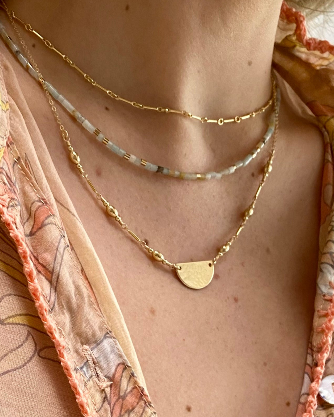 Necklace with a gold chain and pendant on a person wearing a patterned garment.
