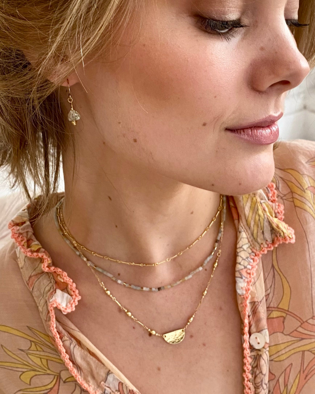 Close-up of a woman wearing multiple gold necklaces and earrings.