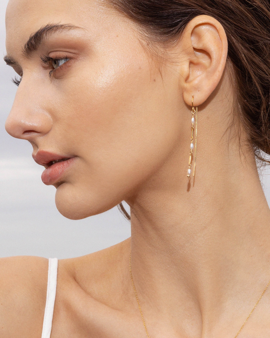 Close-up of a woman wearing gold pearl beaded earrings with a neutral background