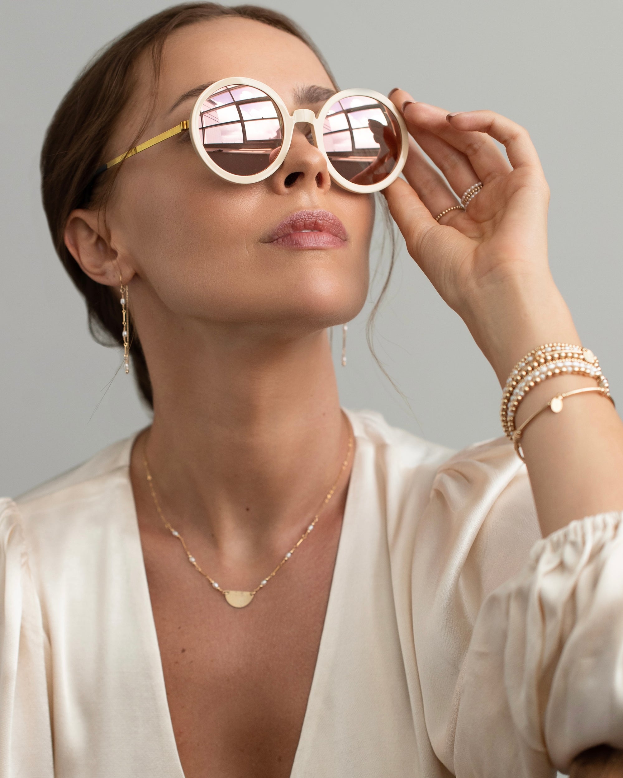 Woman wearing gold and pearl jewellery with stylish Lindberg sunglasses with a neutral background