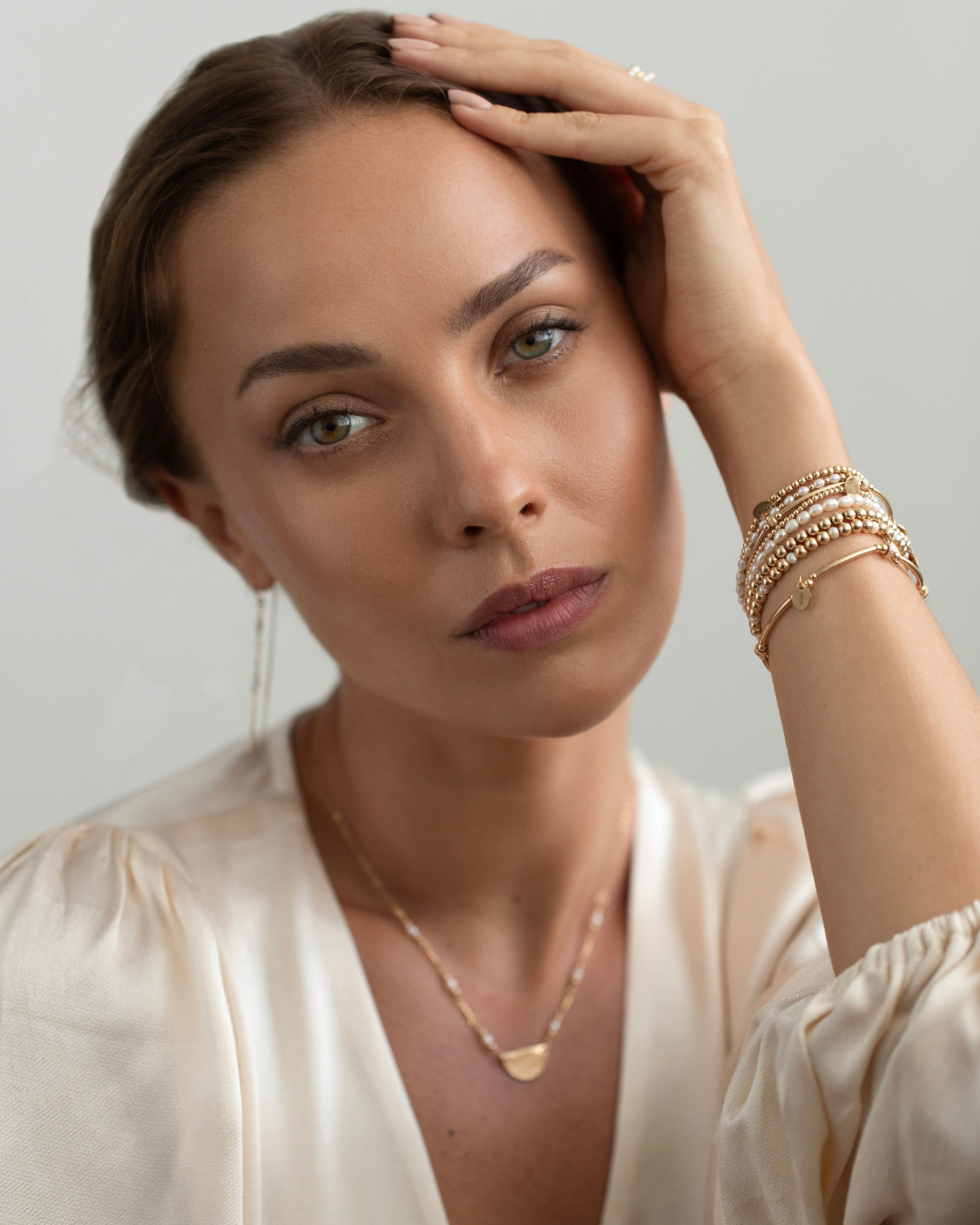 Woman wearing gold jewelry against a neutral background