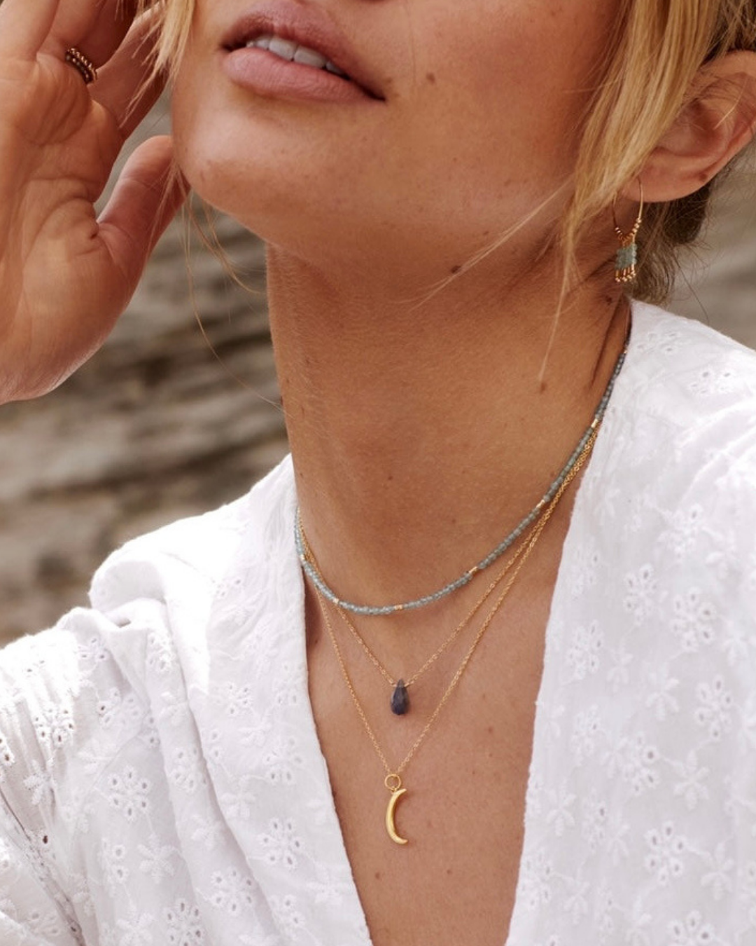 Close-up of a woman wearing multiple necklaces with a blurred natural background