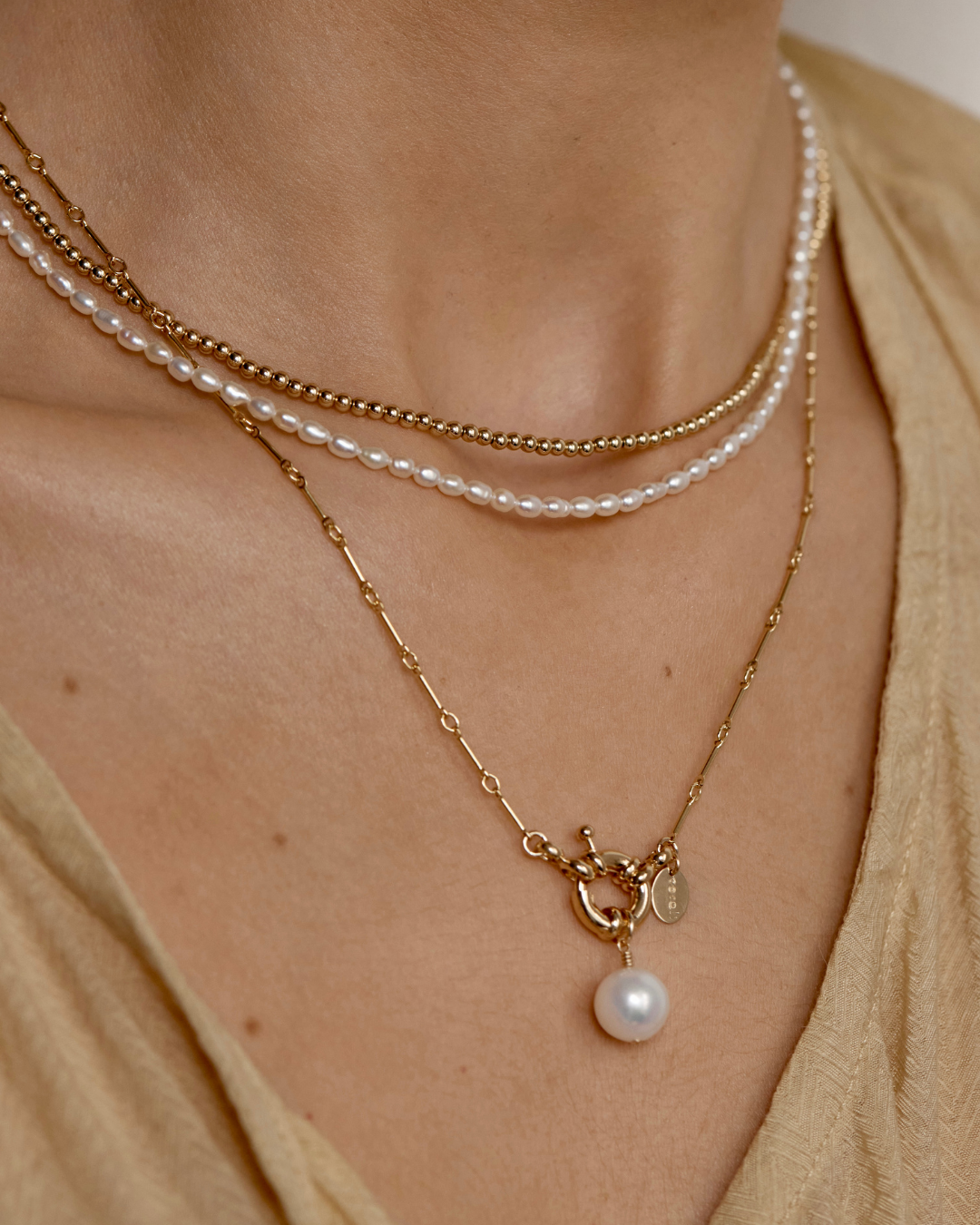 Close-up of layered pearl and gold necklaces on a person wearing a beige top.