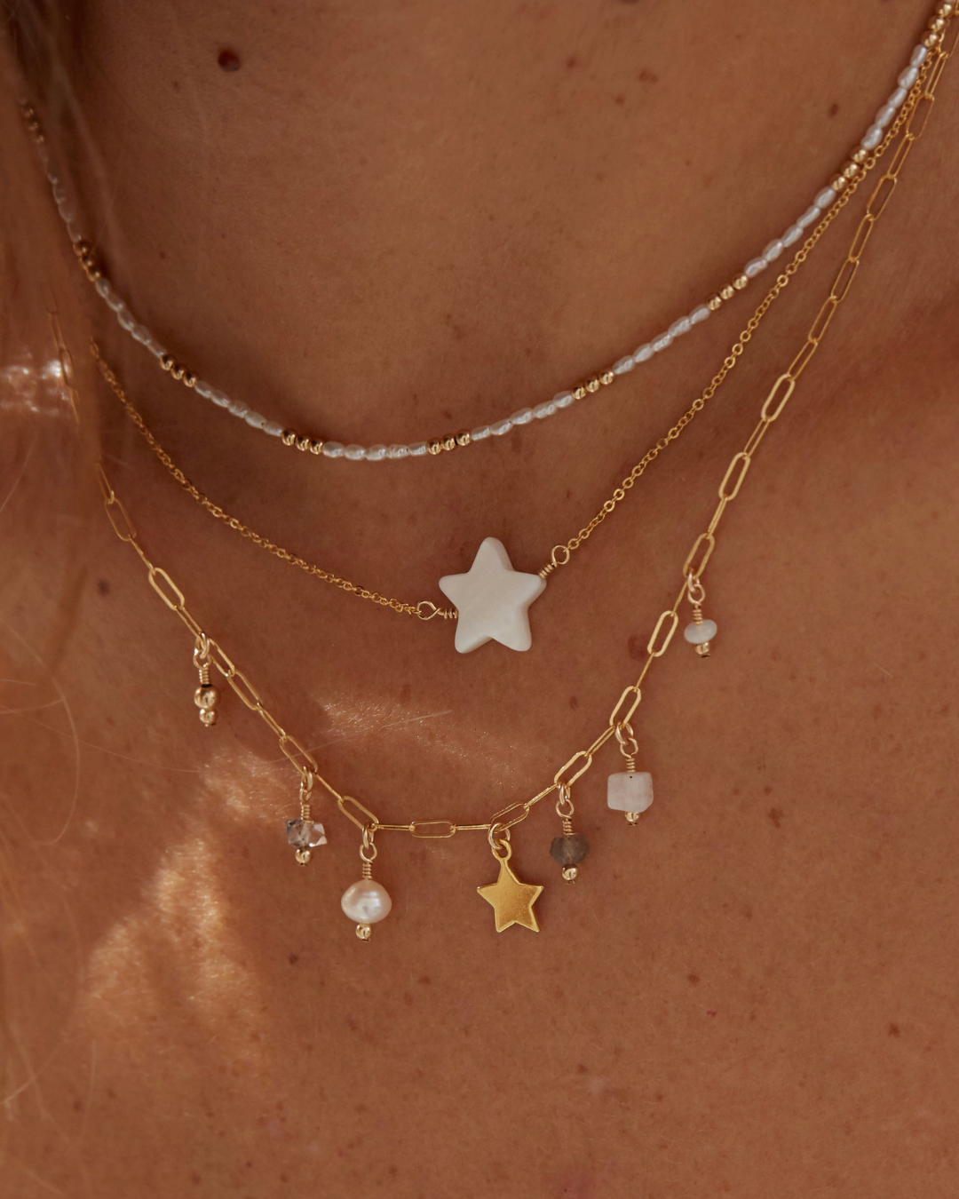 Close-up of a person wearing multiple gold necklaces with mother of pearl star and bead pendants.