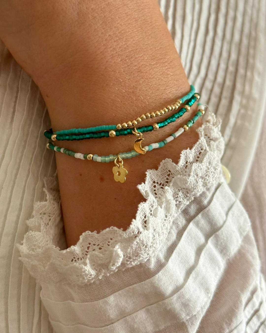Close-up of a wrist wearing multiple turquoise and gold beaded bracelets with a white lace garment.
