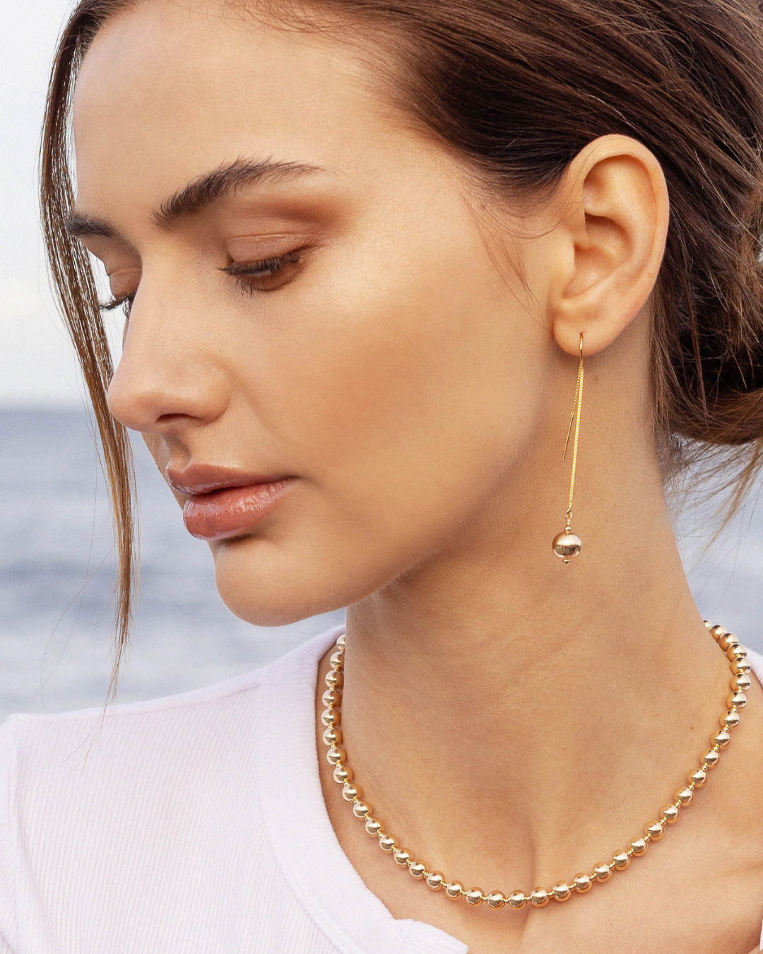 Close up of woman wearing gold necklace and earrings.