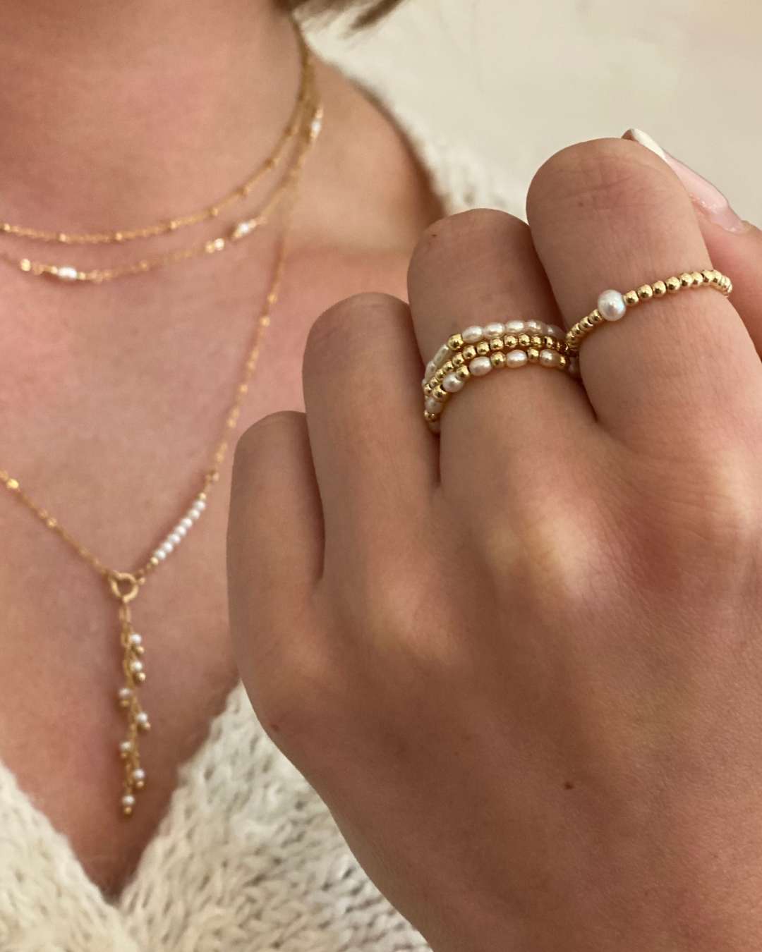 Close-up of a hand wearing gold and pearl jewelry including rings and a necklace.