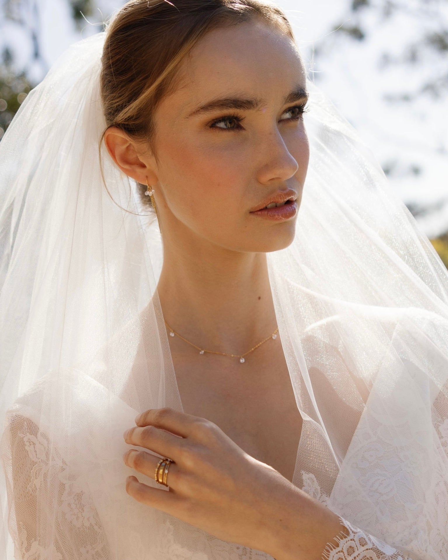 Bride wearing a white lace wedding dress with a veil, outdoors and jewellery