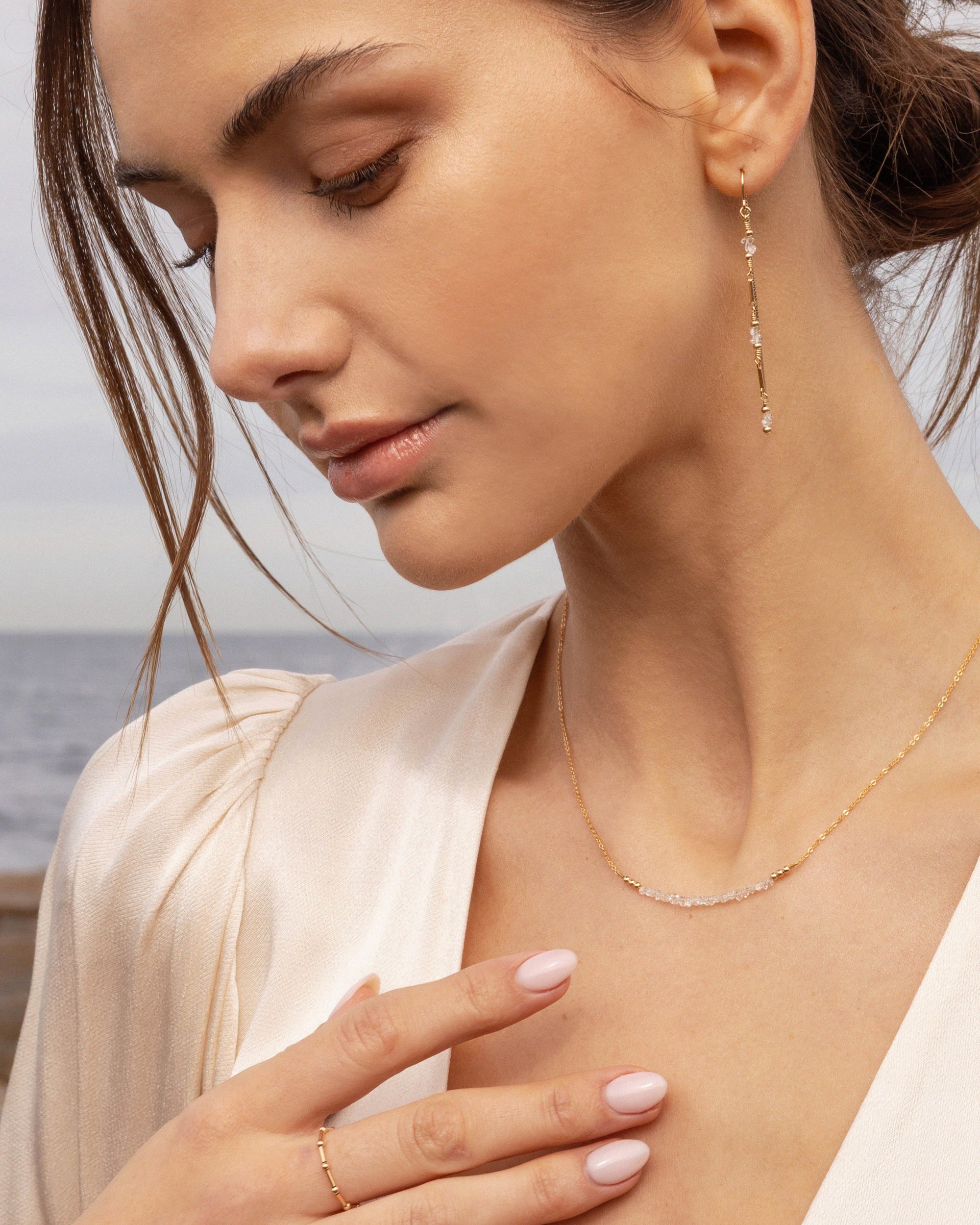 Woman wearing gold and herkimer diamond earrings and necklace by the sea