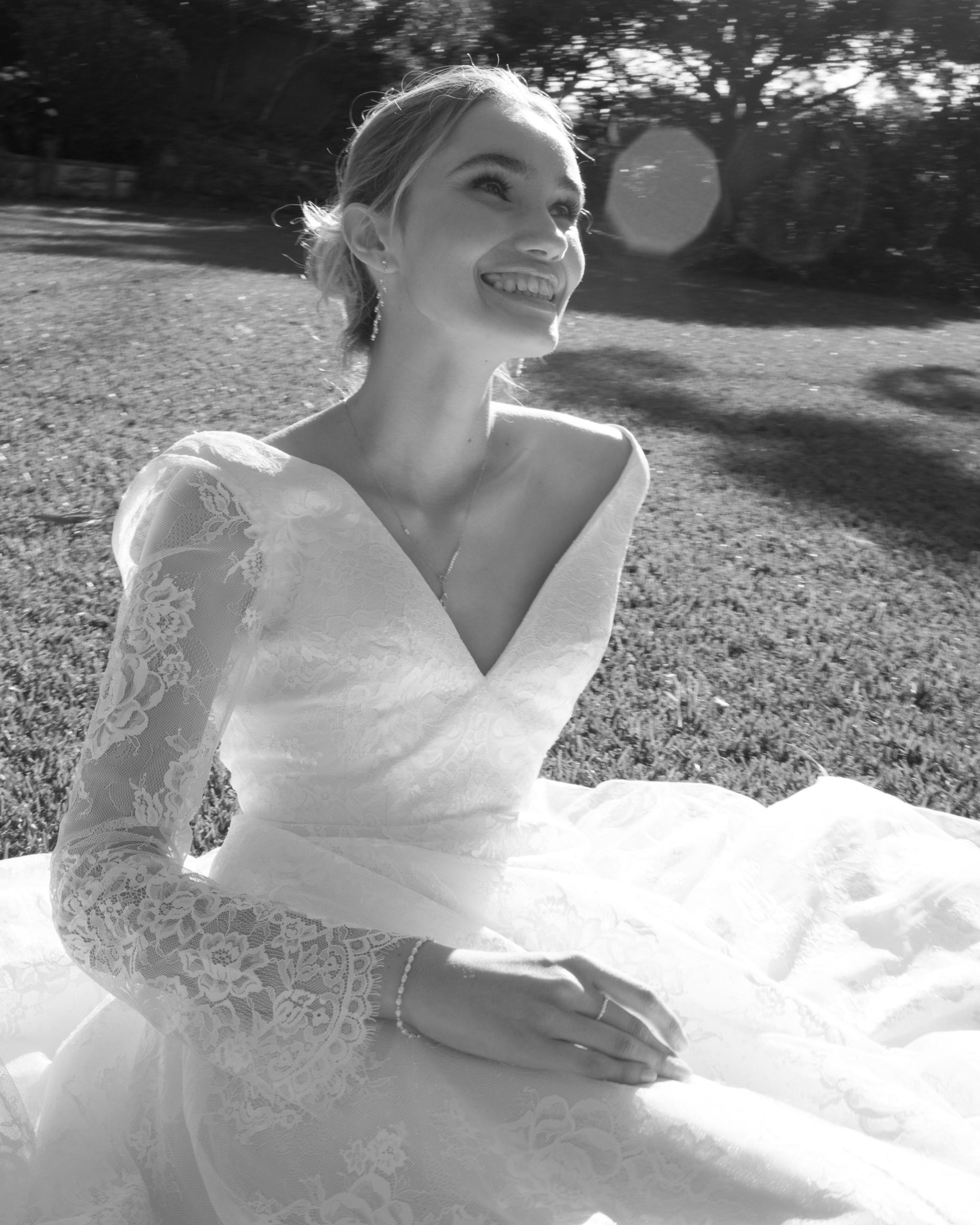 Woman in a wedding dress wearing sitting outdoors with a blurred background.