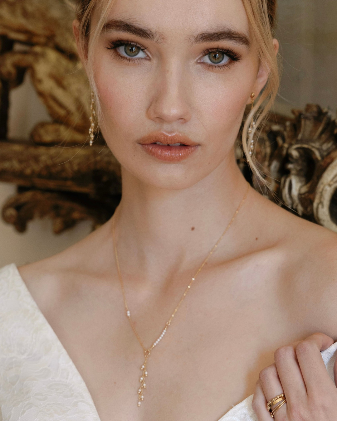 Bride wearing a delicate gold necklace and earrings  with a neutral background