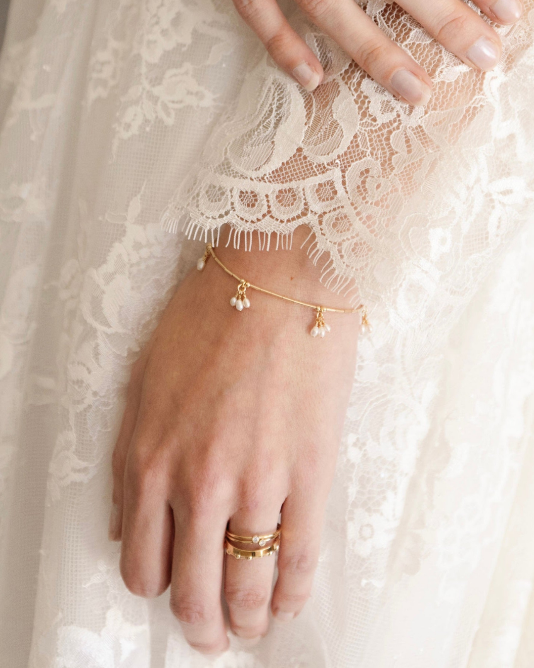 Hand of bride in lace wedding dress wearing gold and pearl jewellery.