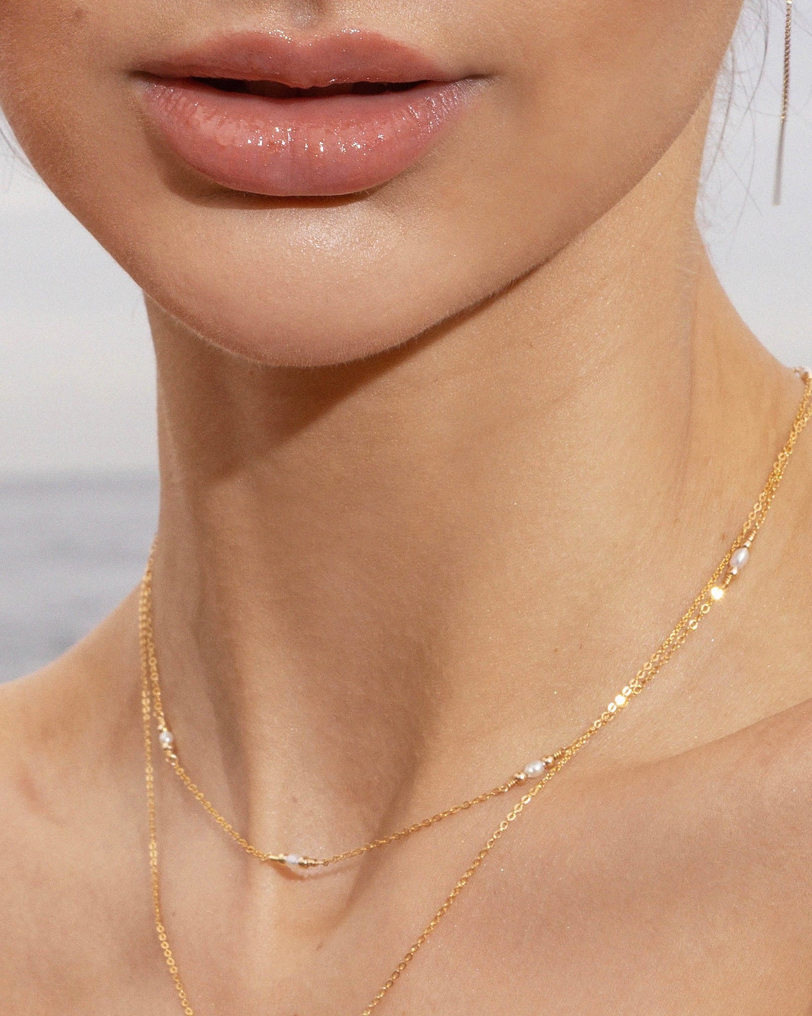 Woman wearing a pearl gold necklace against a neutral background