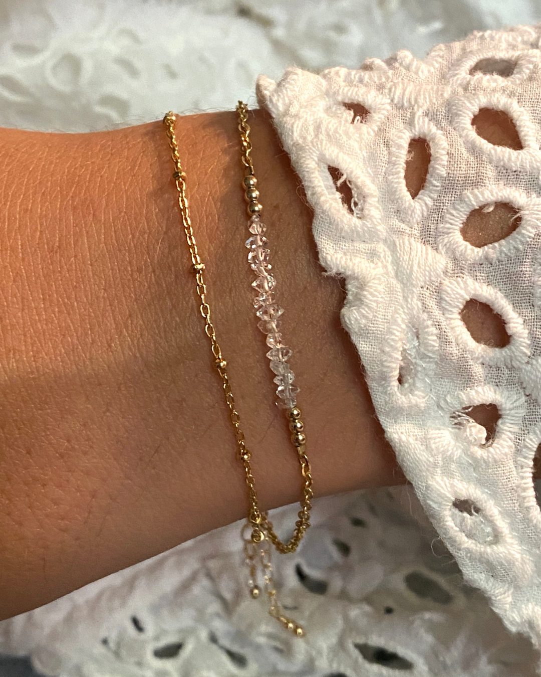 Gold chain and herkimer diamond bracelet  on a wrist against white lace clothing.