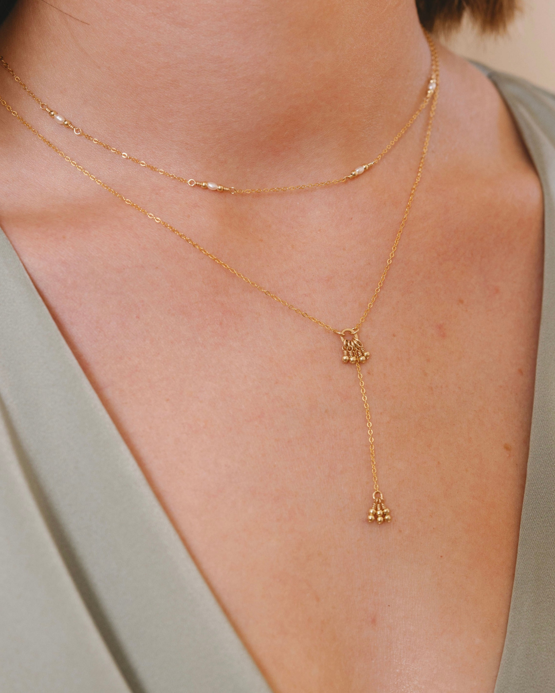 Gold necklace with a pendant on a person wearing a green top.