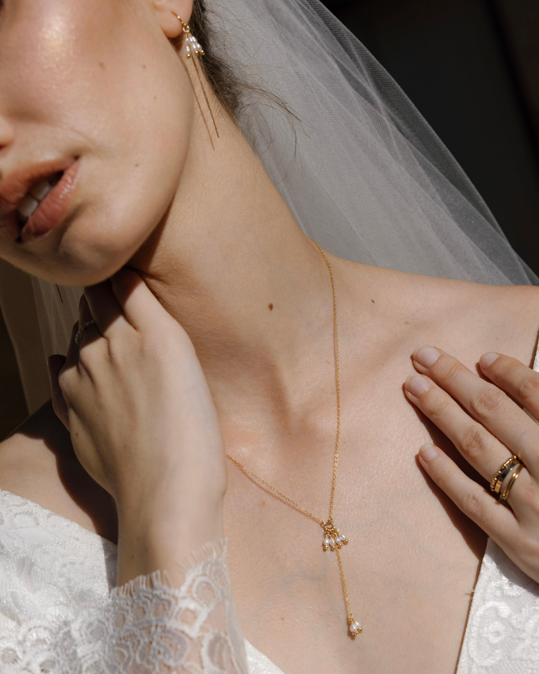 Close-up of a bride wearing a wedding dress and veil and a delicate gold and pearl necklace.