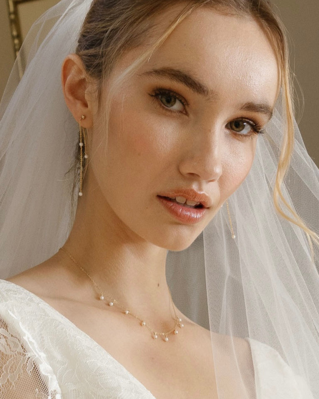 Bride with veil wearing a wedding dress and pearl and gold jewellery.
