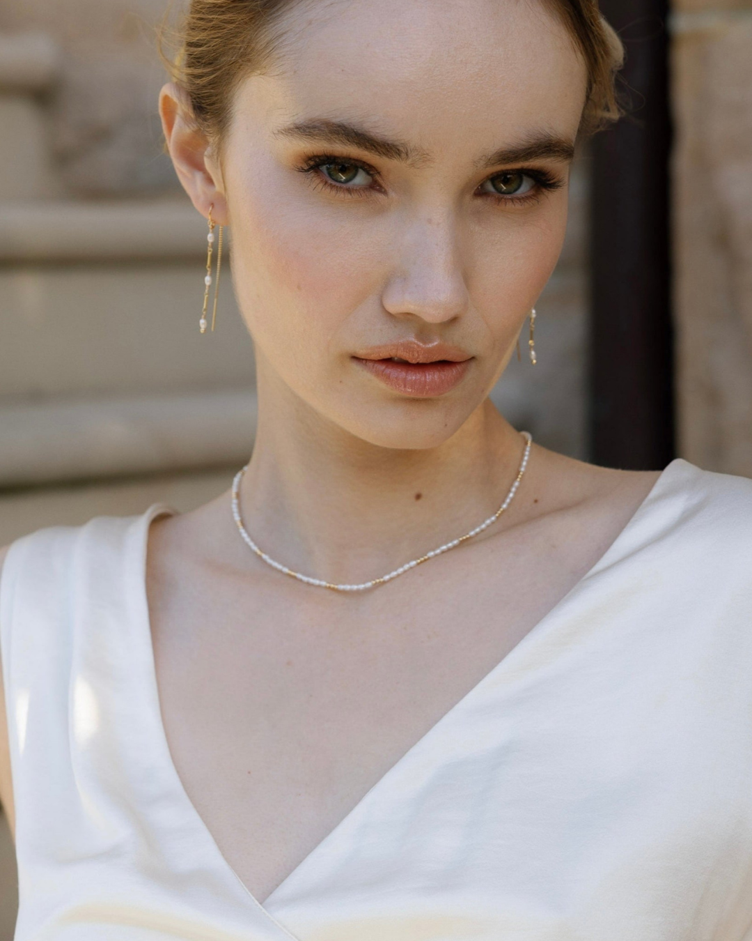 Bride wearing a gold and pearl necklace and earrings with a neutral background