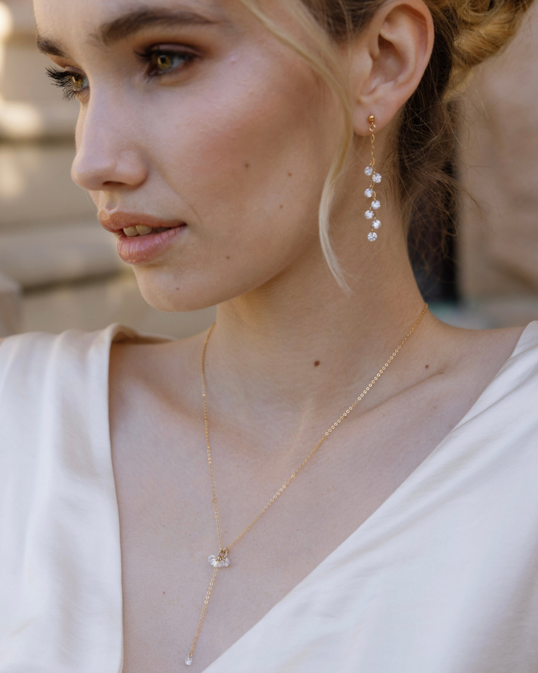 Close-up of a bride in wedding dress wearing gold and Cubic Zirconia Drops earrings and necklace with a blurred background