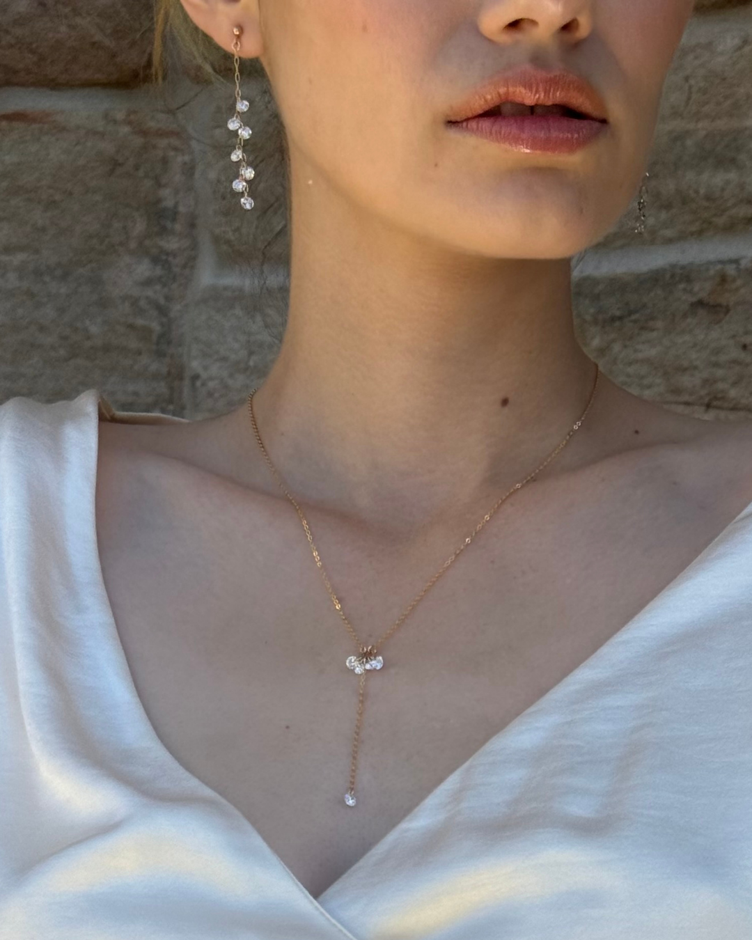 Close-up of a bride wearing a delicate necklace and earrings with gold and Cubic Zirconia Drops.