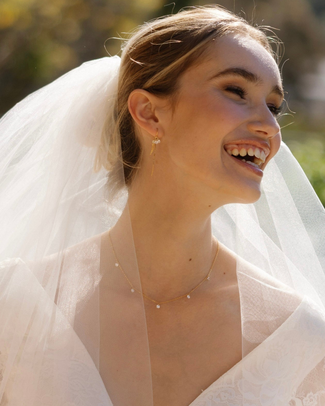 Bride wearing a wedding dress and veil with gold jewellery outdoors