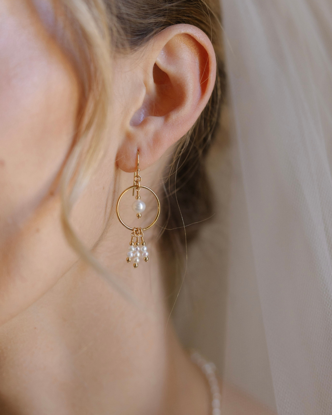 Gold hoop earring with pearl drops worn by a person.