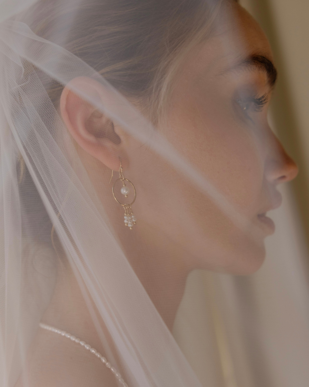 Close-up of a woman wearing a delicate earring with a veil in the background