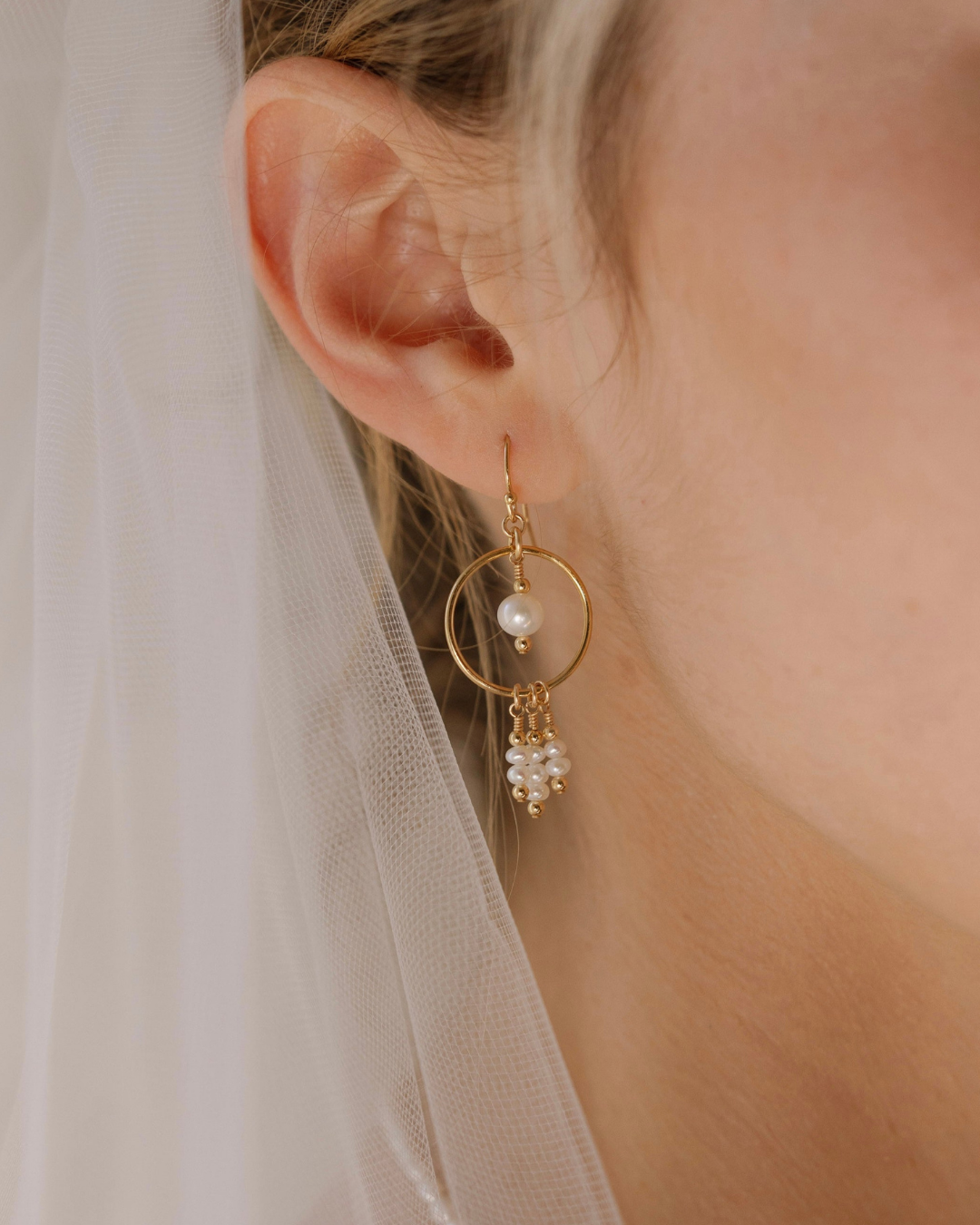 Close-up of a bride's ear wearing gold earrings with pearls, blurred background