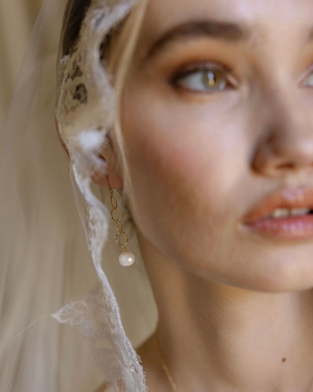 Close-up of a bride in veil wearing pearl earrings with a soft focus on her face and veil.