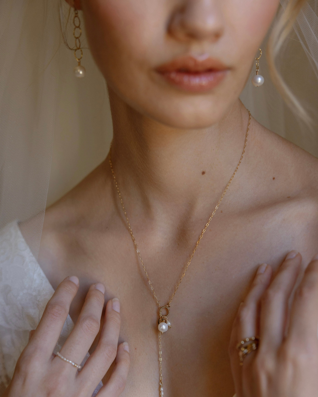 Close-up of a person wearing a gold necklace with a pearl pendant, with a soft blurred background.