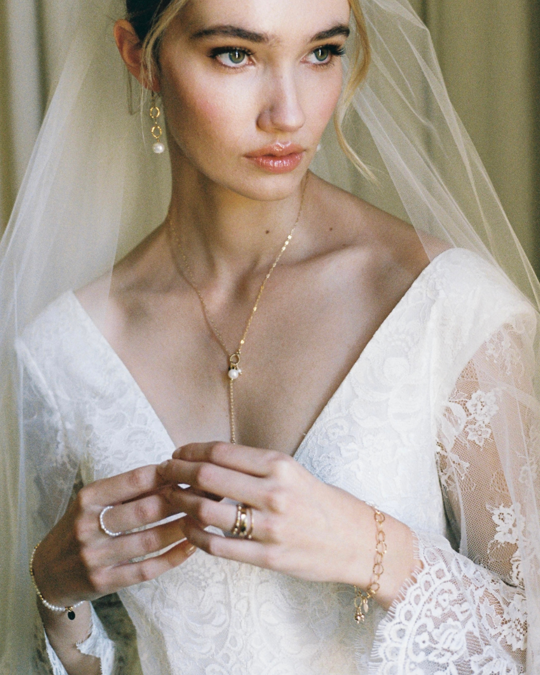 Bride wearing a white lace dress with a veil, gold necklace, and rings.