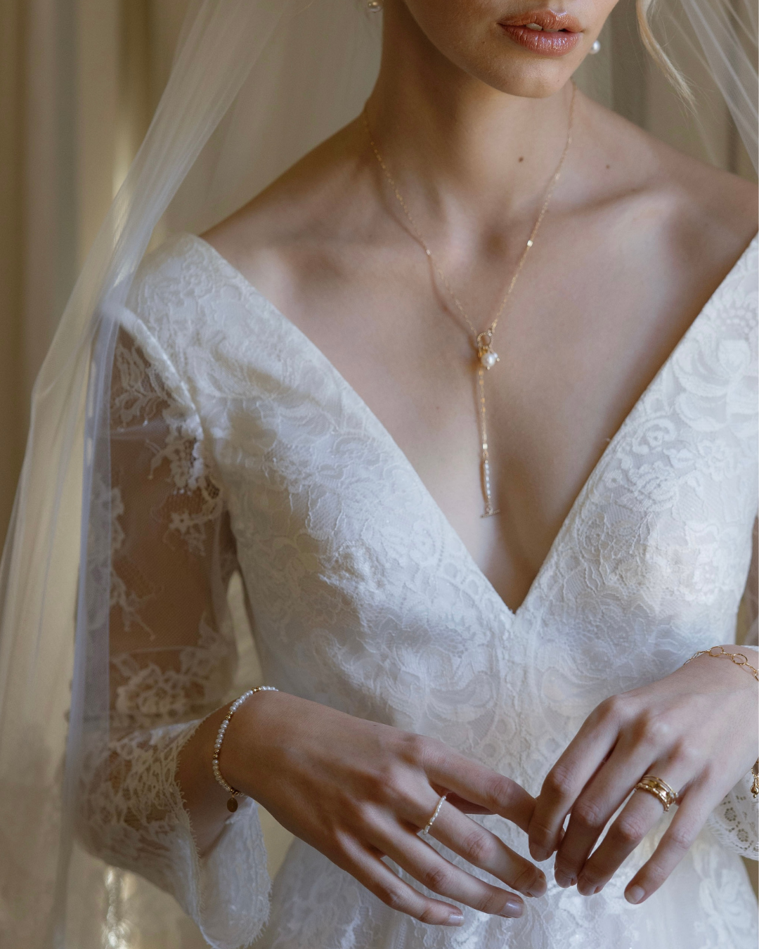 Close-up of a bride wearing delicate necklace and rings, with a soft focus on the background.