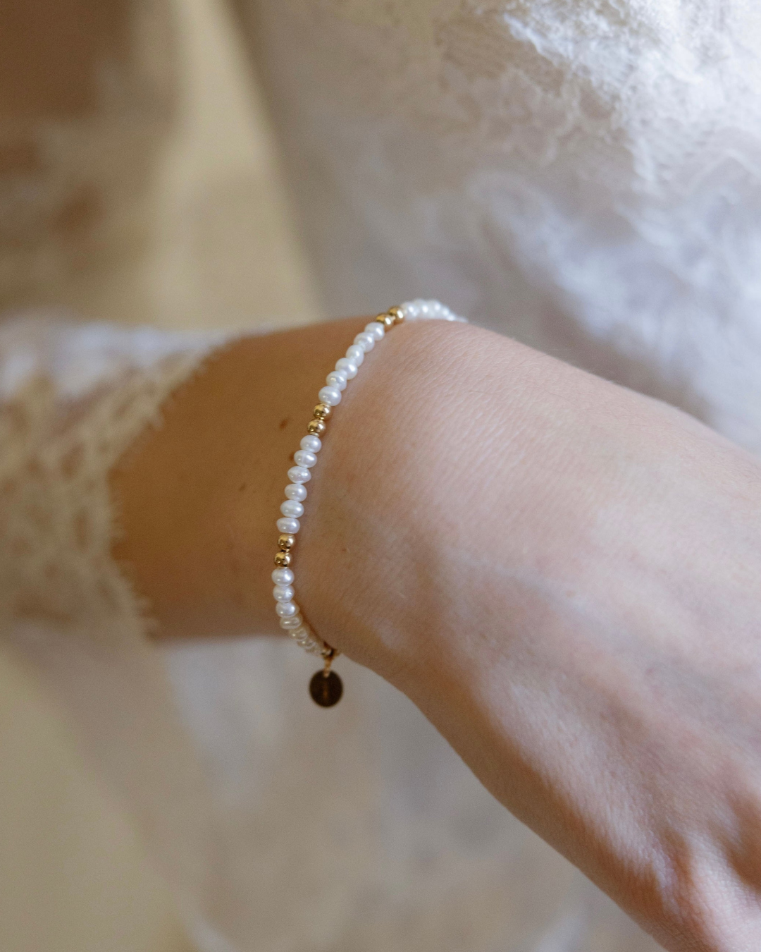 Close-up of a bride's wrist wearing a delicate pearl bracelet with a blurred background