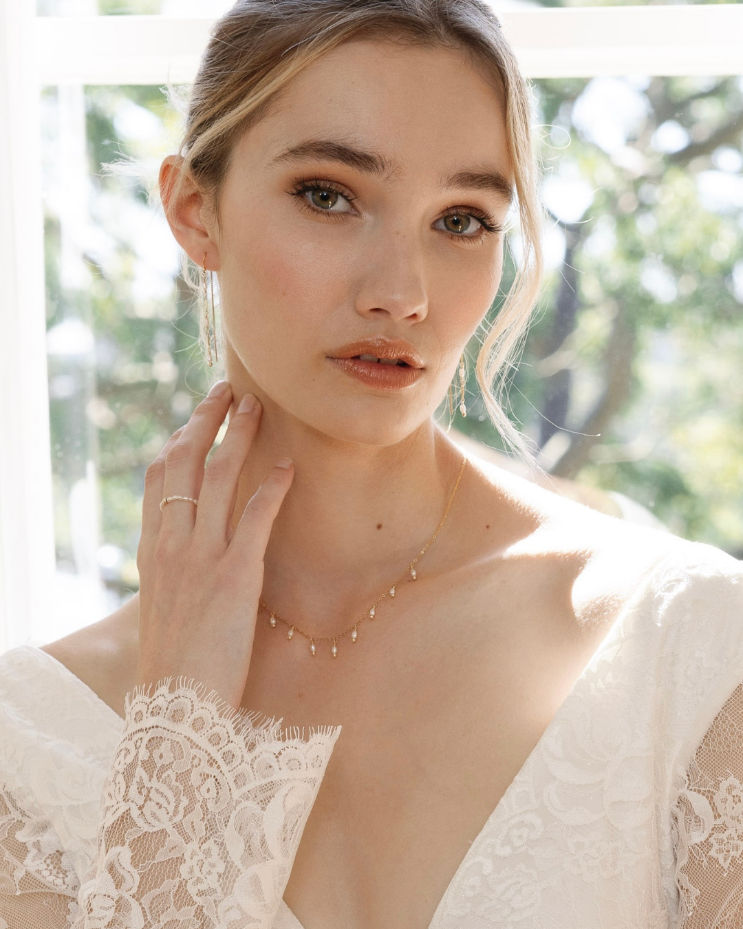 Bride wearing a delicate necklace with a blurred natural background