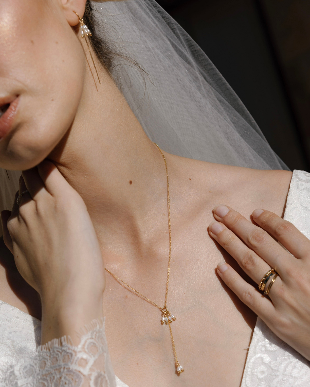 Close-up of a bride wearing a delicate gold and pearl necklace with a blurred background