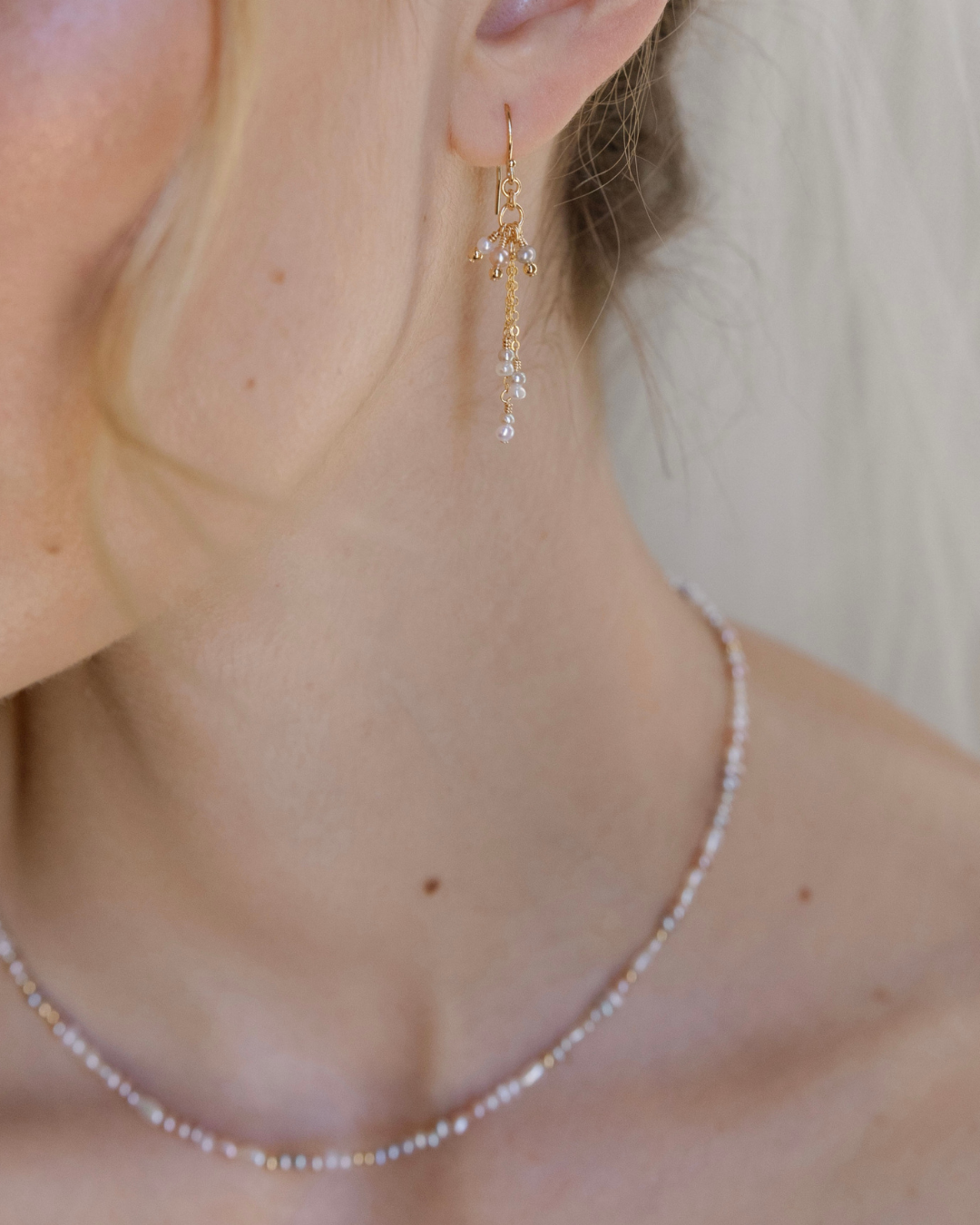 Close-up of a person wearing gold and pearl earrings with a blurred background