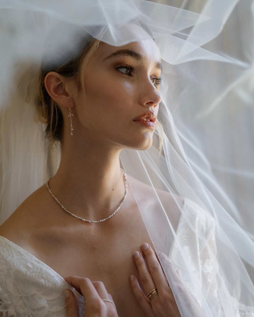 Woman wearing a white wedding dress with a veil, pearl necklace, and ring.