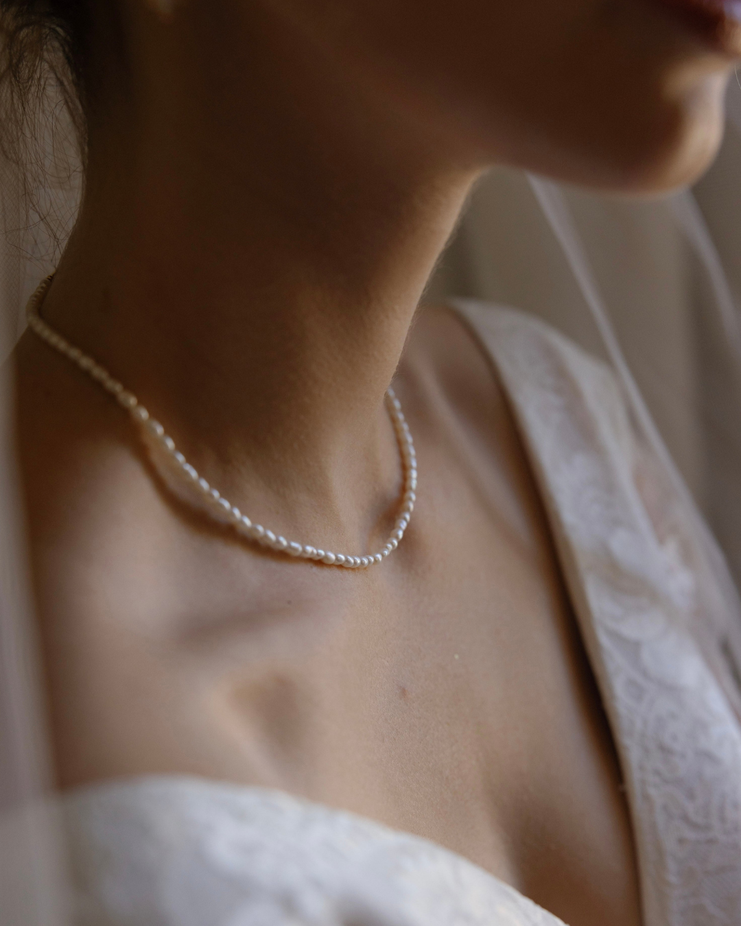 Close-up of a pearl necklace on a person wearing a white lace garment.