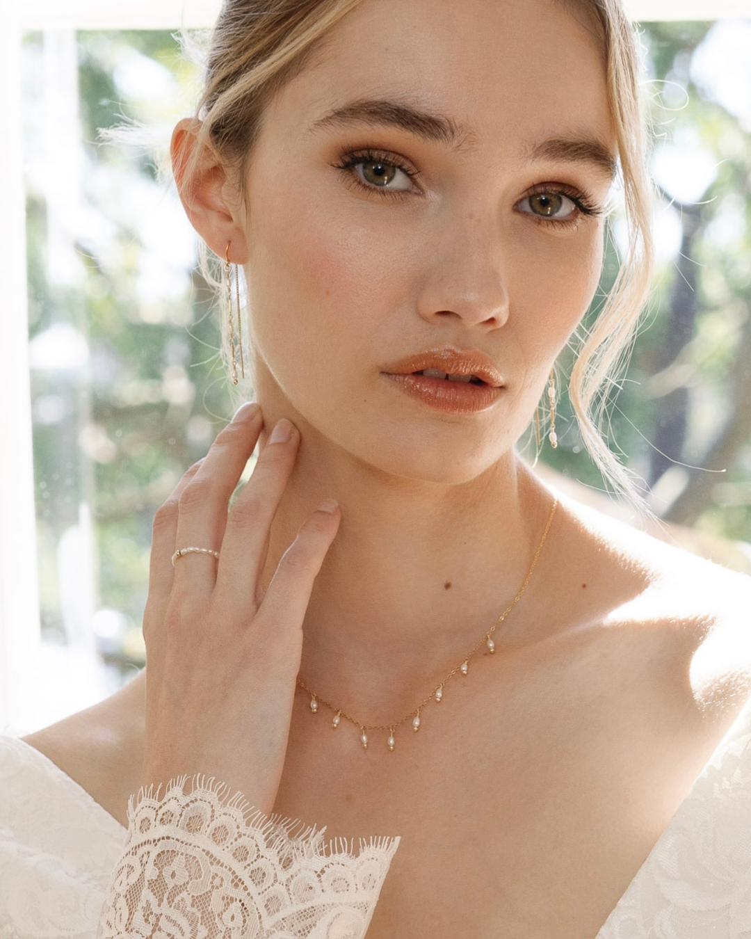 Woman wearing a delicate gold and pearl necklace and ring with a blurred natural background