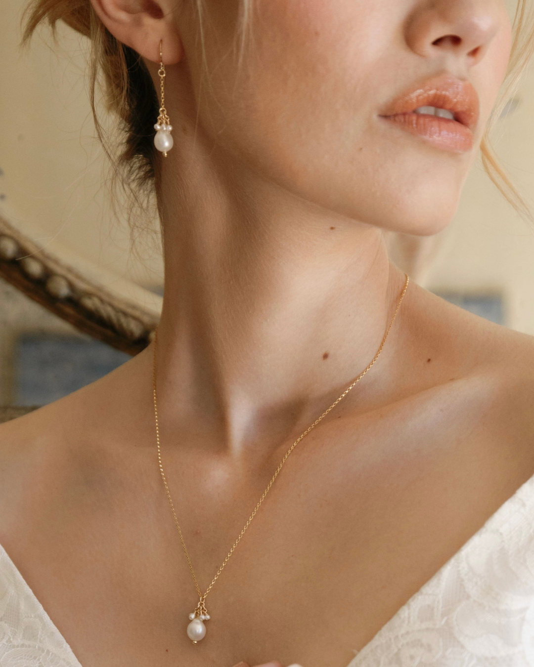 Close-up of a woman wearing a gold necklace with pearl pendant and gold an pearl earrings.