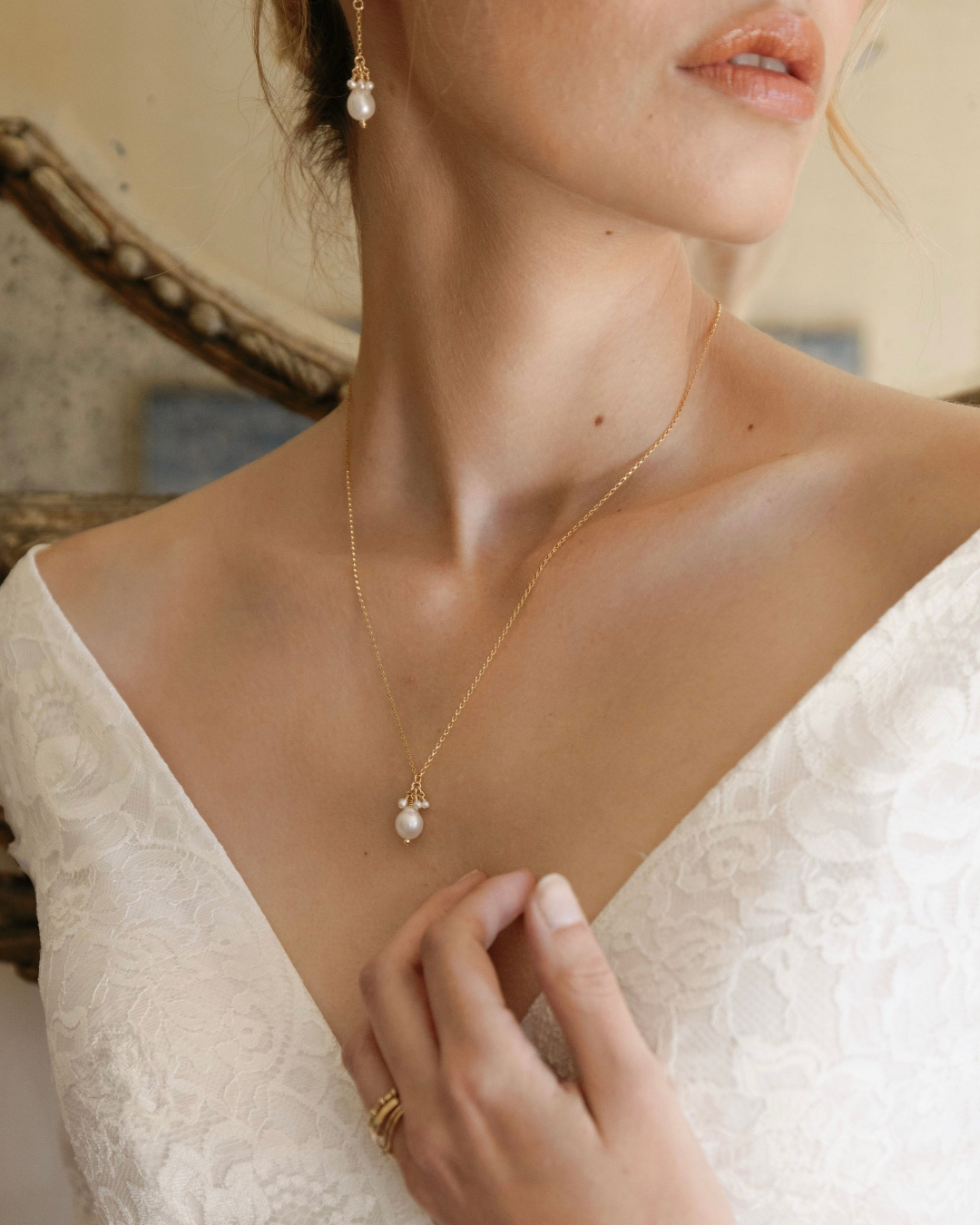 Bride wearing a gold necklace with a pearl pendant, close-up of neck and chest.